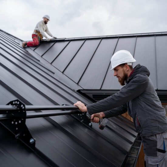 Two roofers installing dark metal roof panels on a residential house.